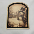 Snowman in snow covered village with two tone arched frame